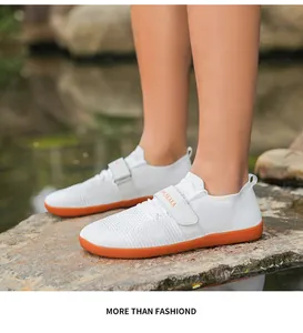 Close-up of white knit training shoes with orange sole and velcro strap on rocks