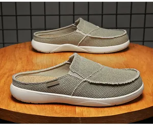 Olivgrüne Canvas-Mules mit Fransen und dicker weißer Gummisohle auf einem Holzständer