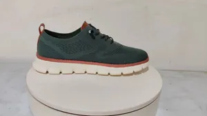 Detailed side view of green breathable knit loafers with premium brown leather accents