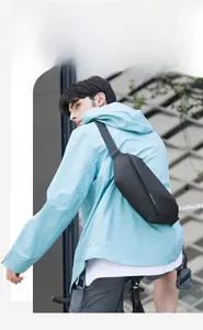Close-up of a black waterproof crossbody sling bag worn over a blue outdoor jacket