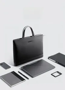 Flat lay of black leather laptop bag with organized office accessories on grey background
