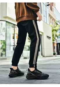 Gros plan sur un jogging noir à bandes latérales et baskets techwear sur le trottoir