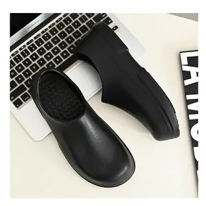 Top view of black non-slip chef shoes on a modern white desk with a laptop setup