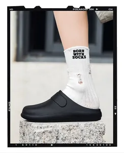 Close-up of matte black chef clogs with white designer socks on stone surface