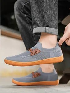 Detail of grey mesh slip-on shoe with orange rubber sole and brown leather patch