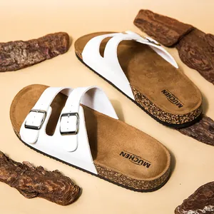 Detailweergave van witte kurken sandalen met dubbele riem en zilveren gespen op schors