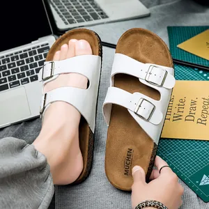 Detailweergave van witte kunstlederen banden met verstelbare metalen gespen op kurken slippers