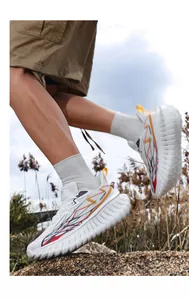 Detail van witte hardloopschoenen met oranje bliksempatronen en grove getande zool
