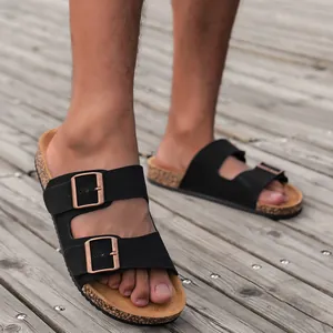 Detailopname van zwarte sandalen met dubbele bandjes en kurken voetbed op een houten dek