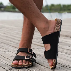 Detail van zwarte suède sandalen met dubbele gesp en kurken zool op een houten terras