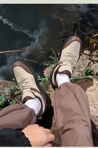 Outdoor close-up of beige men's casual hiking sneakers on rocks near a stream