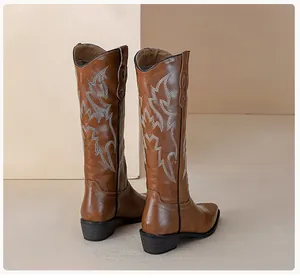 Close-up of retro brown leather cowboy boots featuring white wave embroidery and stable block heels