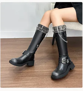 Close-up of black leather boots with denim patchwork, silver chains and metal buckle detail