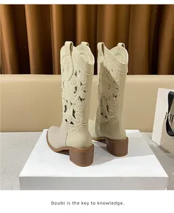 Close-up of cream suede cowboy boots featuring intricate cutout embroidery and stacked heels