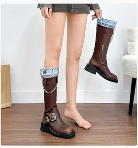 Detail of brown knee-high boots featuring metal chains and denim patchwork trim