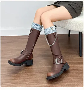 Detail of knee-high boots with denim cuffs, metal chains, and distressed leather texture