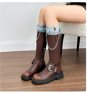 Detail of brown leather biker boots featuring vintage finish, metal chains, and denim cuff