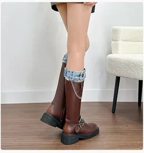 Detail of distressed brown leather boots with denim cuff and decorative metal chain