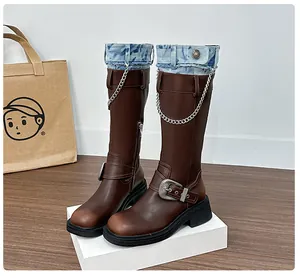 Detail of brown vintage riding boots featuring denim patchwork and silver chain accents