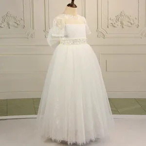 White lace flower girl dress with pearl belt and layered tulle skirt on a vintage background