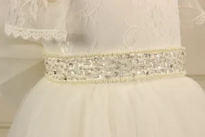Close-up of white lace girl dress featuring pearl waistband and silver sequins detail