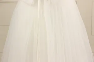 Detailed close-up of white tulle layers, lace embroidery and satin bow on girl's gown