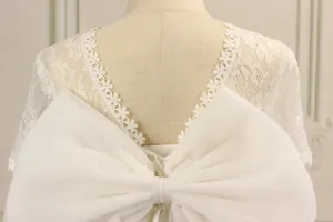 Detail of white lace flower girl dress back with V-neckline and large mesh bow on mannequin