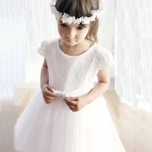 Détail du corsage en dentelle blanche avec boucle en strass sur une robe de mariée enfant