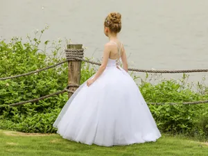 Detail eines weißen Mädchen-Festkleides mit rückenfreien Kreuzträgern und flauschigem Tüllrock