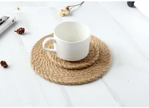 Vue détaillée des sets de table ronds en jute superposés sur une table en bois blanc