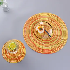 Set of round woven cotton table mats in orange and yellow spiral patterns on grey surface