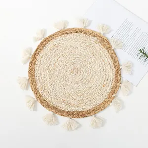 Close-up of a round hand-woven grass placemat with cream tassels and natural texture
