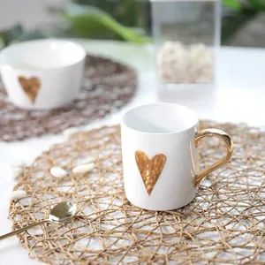 Detail of white ceramic mug with gold heart pattern on a woven round placement