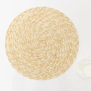 Detailed top view of a handwoven round straw placemat with spiral texture and water glass