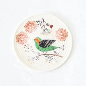 Top view of a round woven cotton placemat featuring a green bird and floral print details