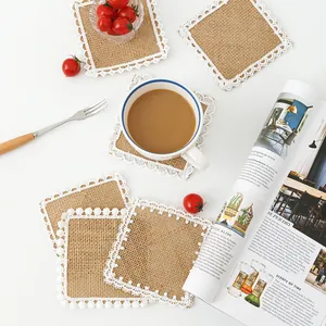 Detail view of square jute coaster with white lace fringe and decorative pom-poms