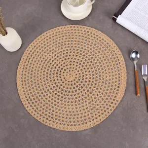 Top view of a round woven jute placemat on a dark stone table with tableware