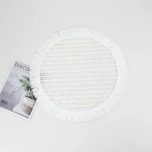 Close-up of a white woven round placemat with fringe details and hollow grid texture