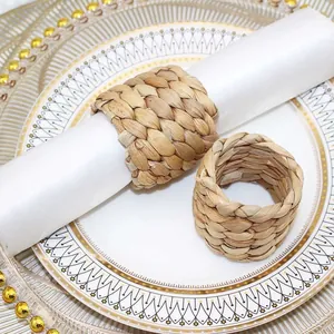 Detalle de servilleteros de paja natural tejida a mano sobre elegantes platos de borde dorado