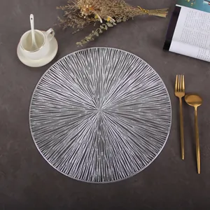 Close-up of silver round hollow placemat with sunburst design on dark tabletop