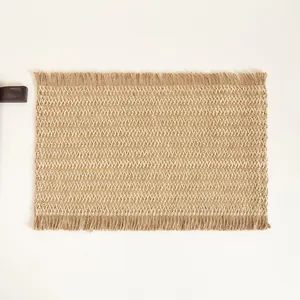 Detail of woven jute place mat with zigzag texture and natural fringe edges on beige background