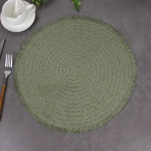 Overhead view of sage green woven placemat with delicate fringe on a stone surface