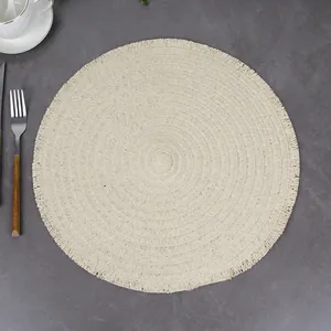 Close-up of beige woven round placemat with fringe details and dense spiral texture