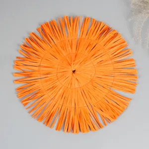 Macro detail of round orange woven paper placemat with stylish fringed tassels