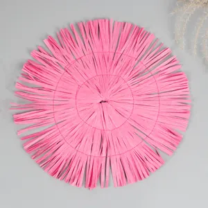 Detailed top view of a pink round woven placemat with fringe and decorative dried grass