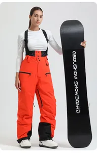 Detail of waterproof orange ski bib pants with black straps and reinforced hem guards