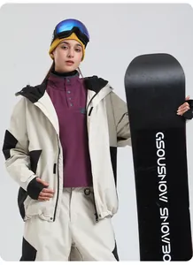 Female model in beige ski jacket and pants with yellow beanie holding a snowboard
