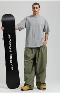 Male model wearing olive green baggy ski pants with a grey t-shirt holding a snowboard