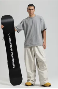 Detail of grey ski top and off-white loose snowboard pants with a black snowboard