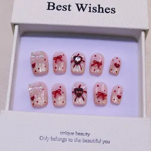 Détails de faux ongles roses avec nœuds rouges et gemmes dans leur boîte cadeau
